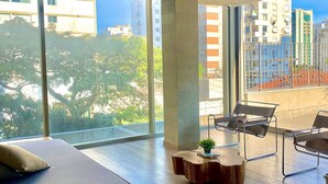 Un dormitorio moderno con una cama grande, una mesa de centro de madera y vistas de la ciudad a través de amplios ventanales.