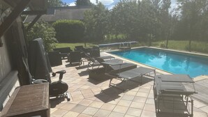 Un patio trasero con piscina, mobiliario exterior y una zona de patio.