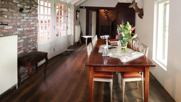 Uma sala de jantar com uma mesa de madeira, cadeiras, um vaso com flores e um chifre de veado fixado na parede.