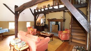Uma sala de estar aconchegante com teto alto, vigas de madeira aparente, lareira e escada.