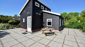 A modern two-story building with a dark exterior, a white door, and a small patio area with a wooden table and chairs. - Holiday Home in Eerbeek near Veluwe (Eerbeek)