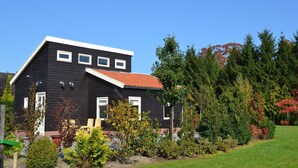 A black house with a red roof, surrounded by greenery and trees. - Holiday Home in Eerbeek near Veluwe (Eerbeek)