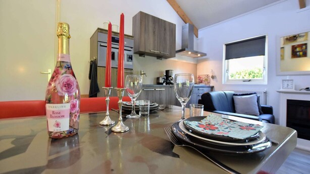 A dining table with a bottle of rose blossom sparkling wine, red candles, and clear glasses. - Holiday Home in Eerbeek near Veluwe (Eerbeek)