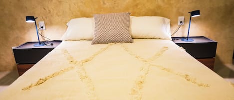 Una cama con un cojín estampado, dos lámparas de noche y una pared con textura.