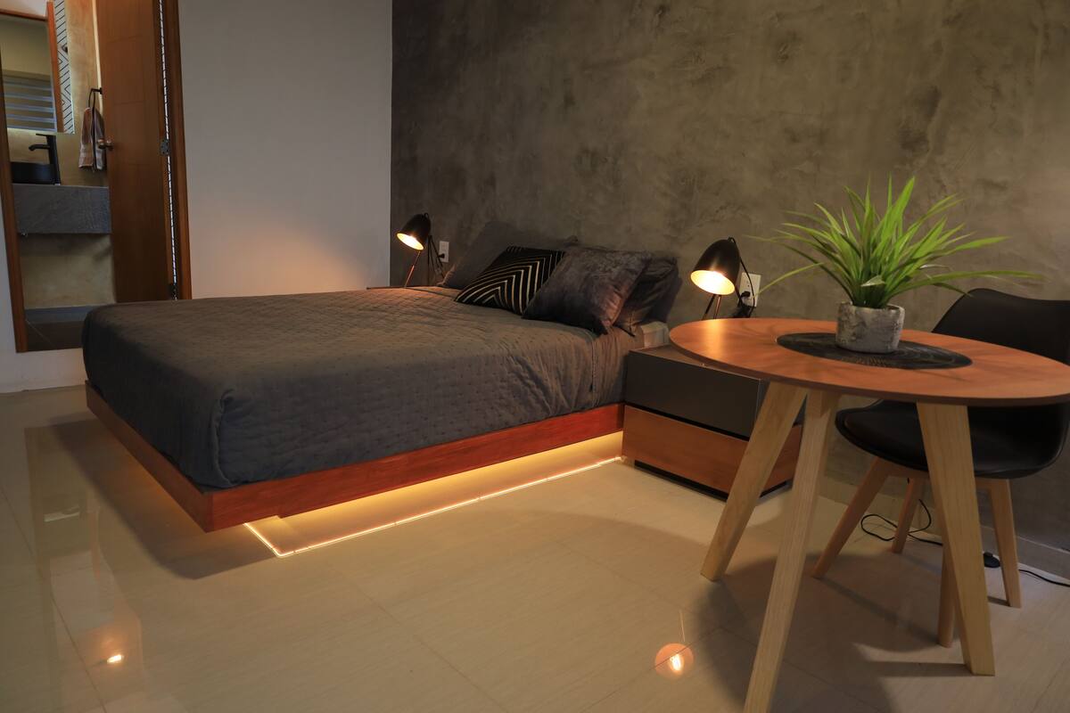Quarto moderno com cama, abajures, uma mesinha com uma planta e uma cadeira.