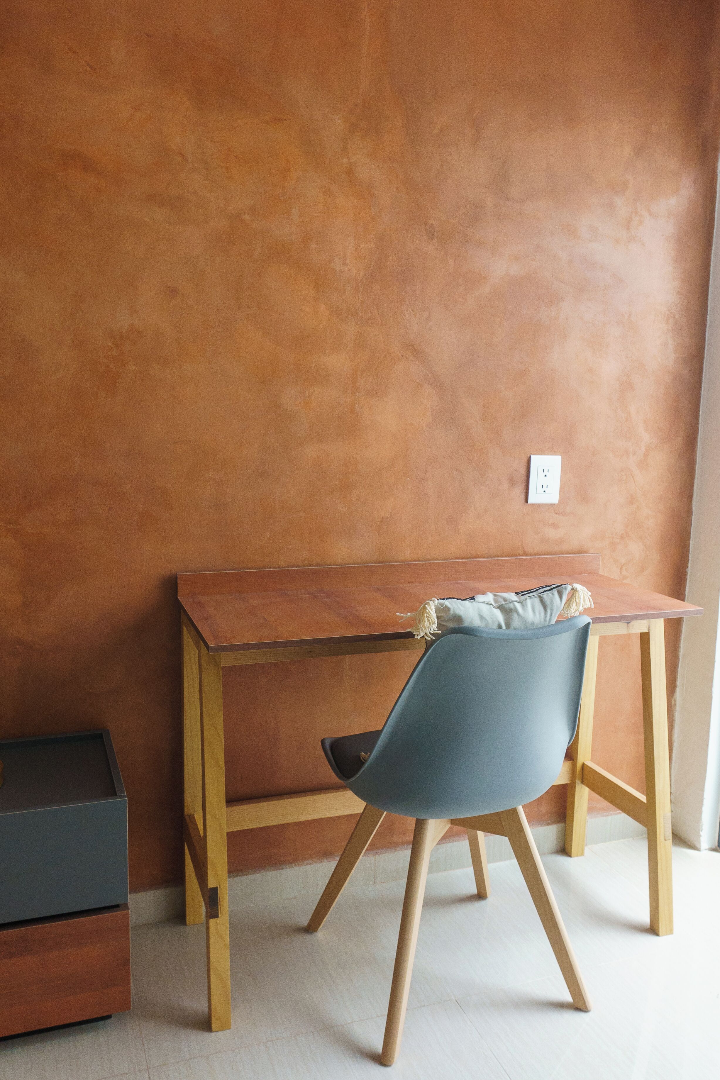 A wooden desk with a blue chair against a textured wall.