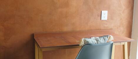 A wooden desk with a blue chair against a textured wall.