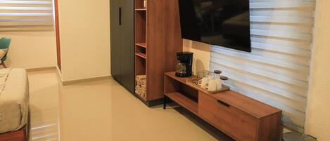 A modern living room with a flat-screen TV mounted on the wall, wooden shelving, a coffee maker, and a small table.