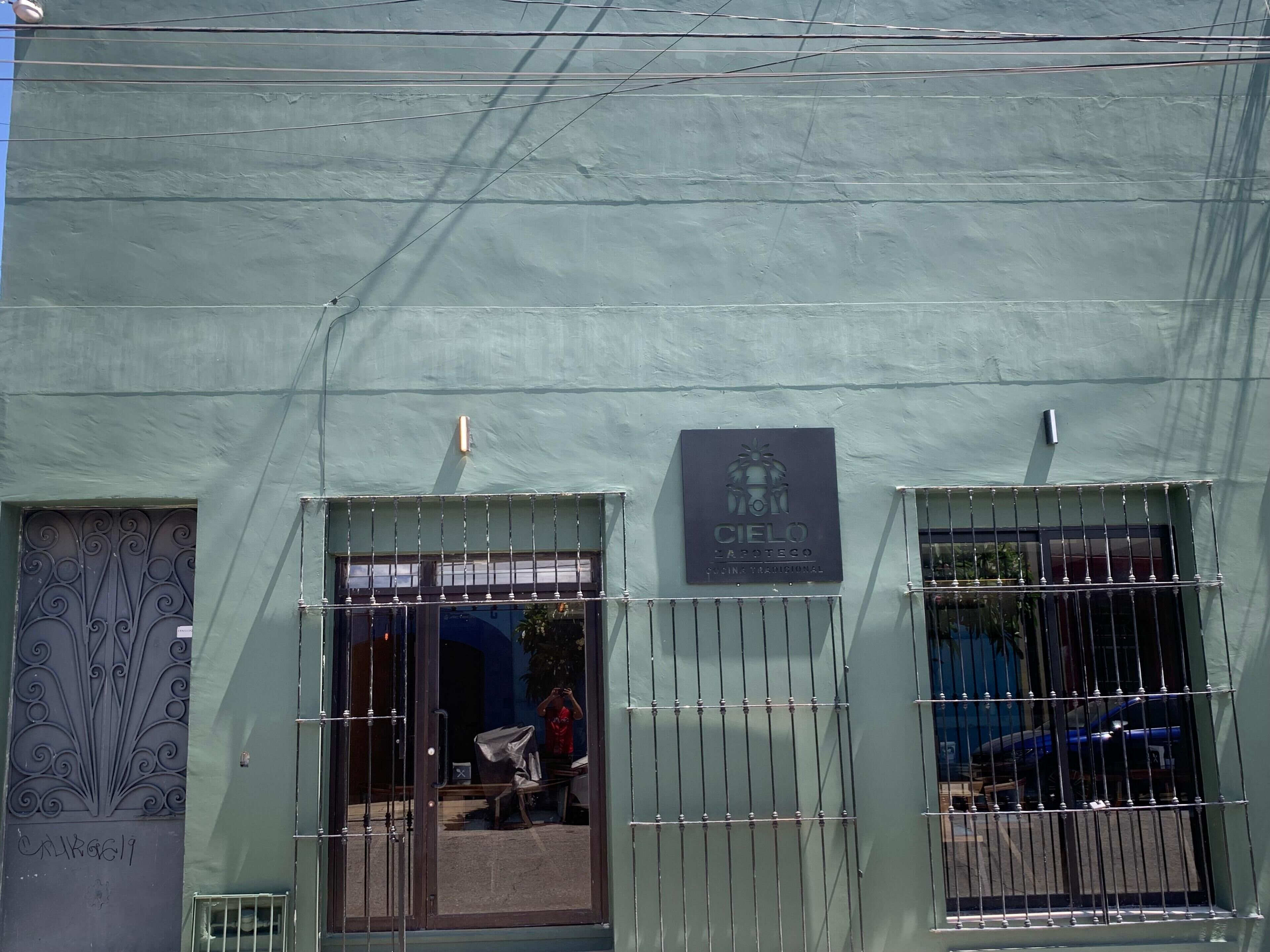 Fachada de edificio con exterior verde, una reja metálica en la entrada y un letrero que dice "Cielo".