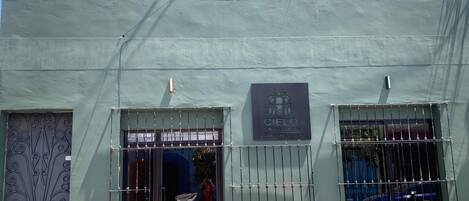 Fachada de edificio con exterior verde, una reja metálica en la entrada y un letrero que dice "Cielo".