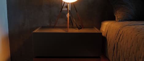 A bedside table with a lamp, a bed with a patterned bedspread, and a textured wall.