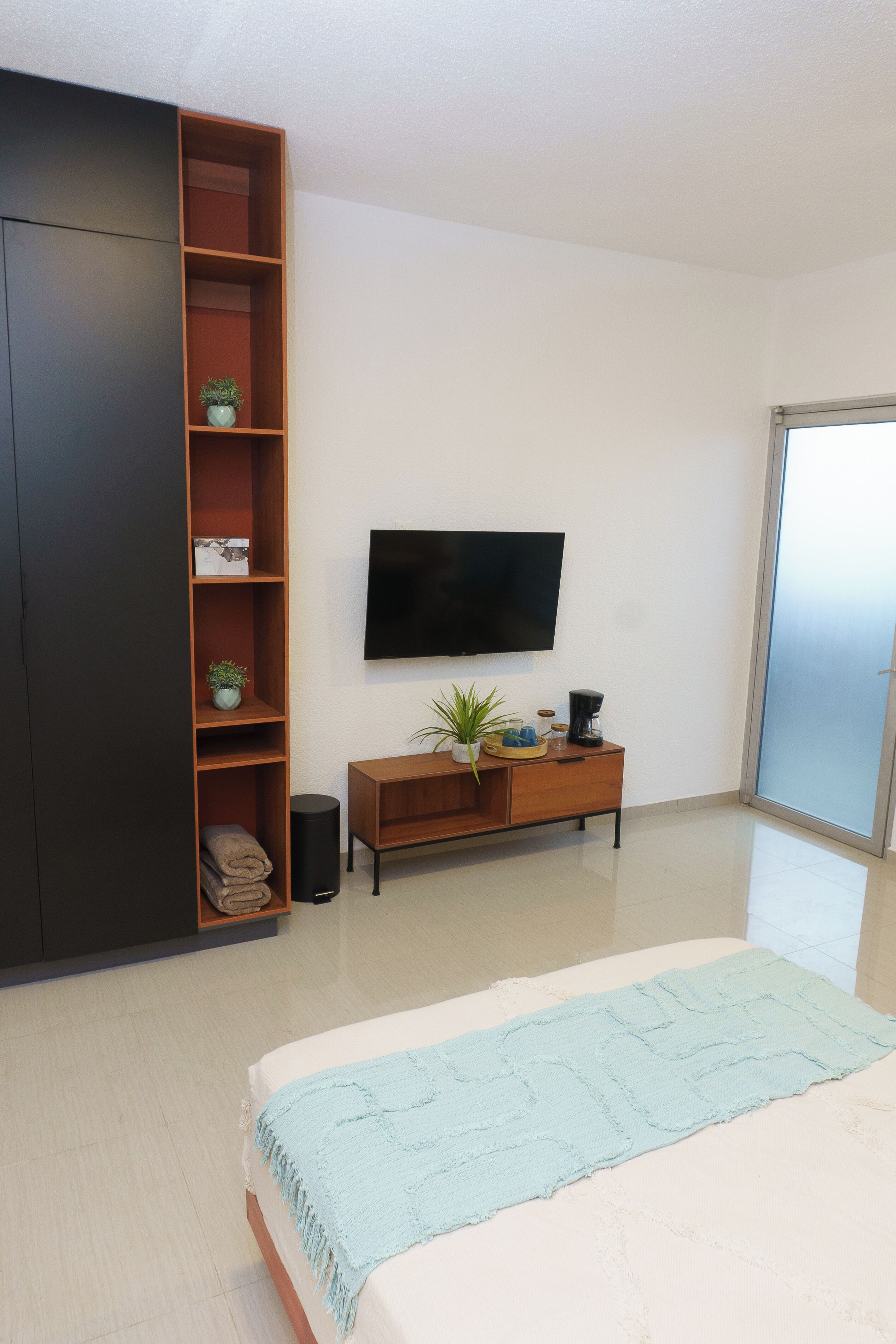A bedroom with a bed, a TV, a wardrobe, a console table, and a sliding glass door.