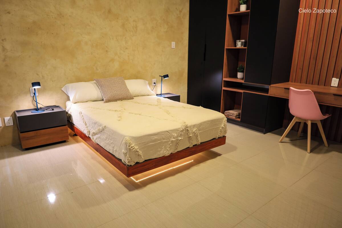 Quarto com cama, mesas de cabeceira, escrivaninha e uma cadeira.