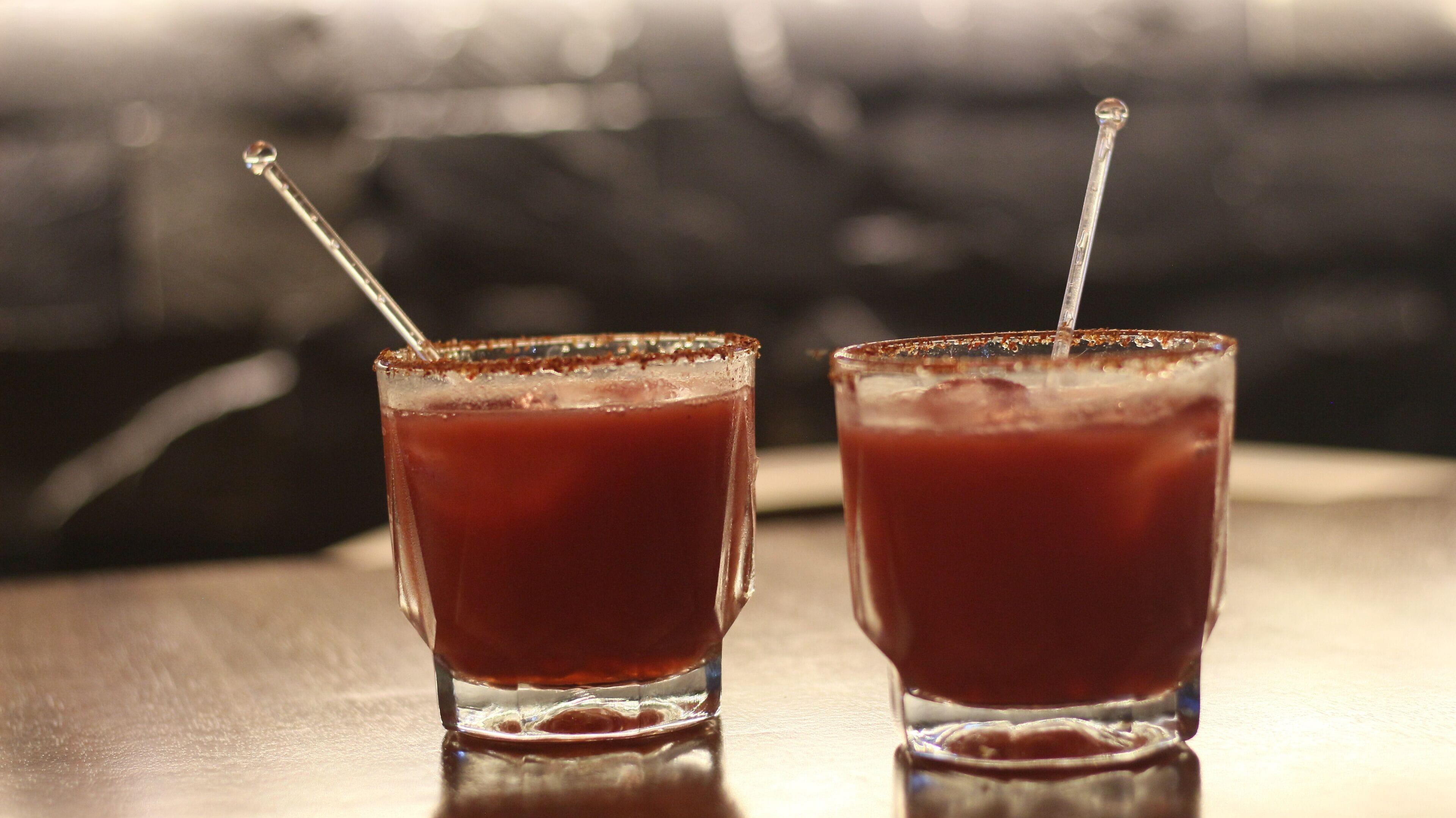 Deux verres d’une boisson rouge, chacun muni d’une paille, sont posés sur une surface réfléchissante.