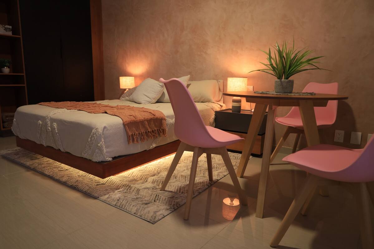 Quarto com cama, mesas de cabeceira, escrivaninha, cadeiras e um vaso de planta.