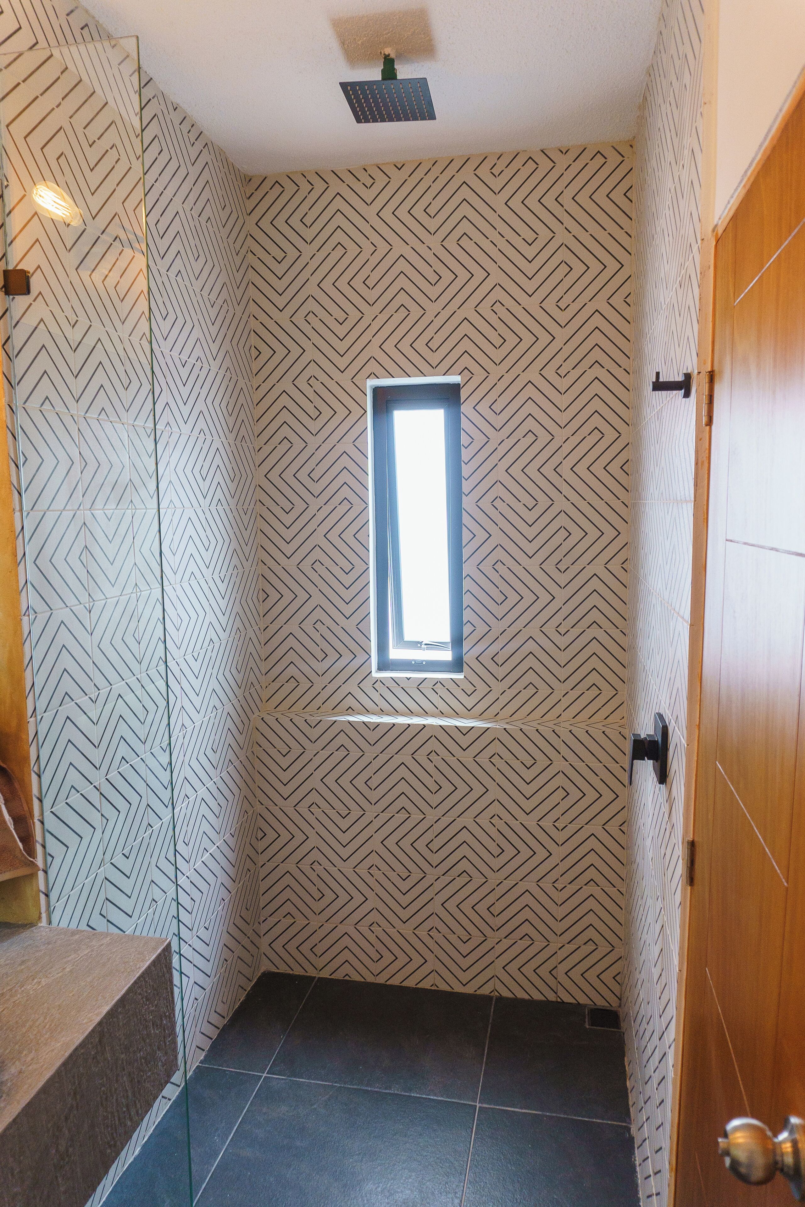 Ein Badezimmer mit Wand in geometrischem Muster, einem kleinen Fenster und einer Holztür.