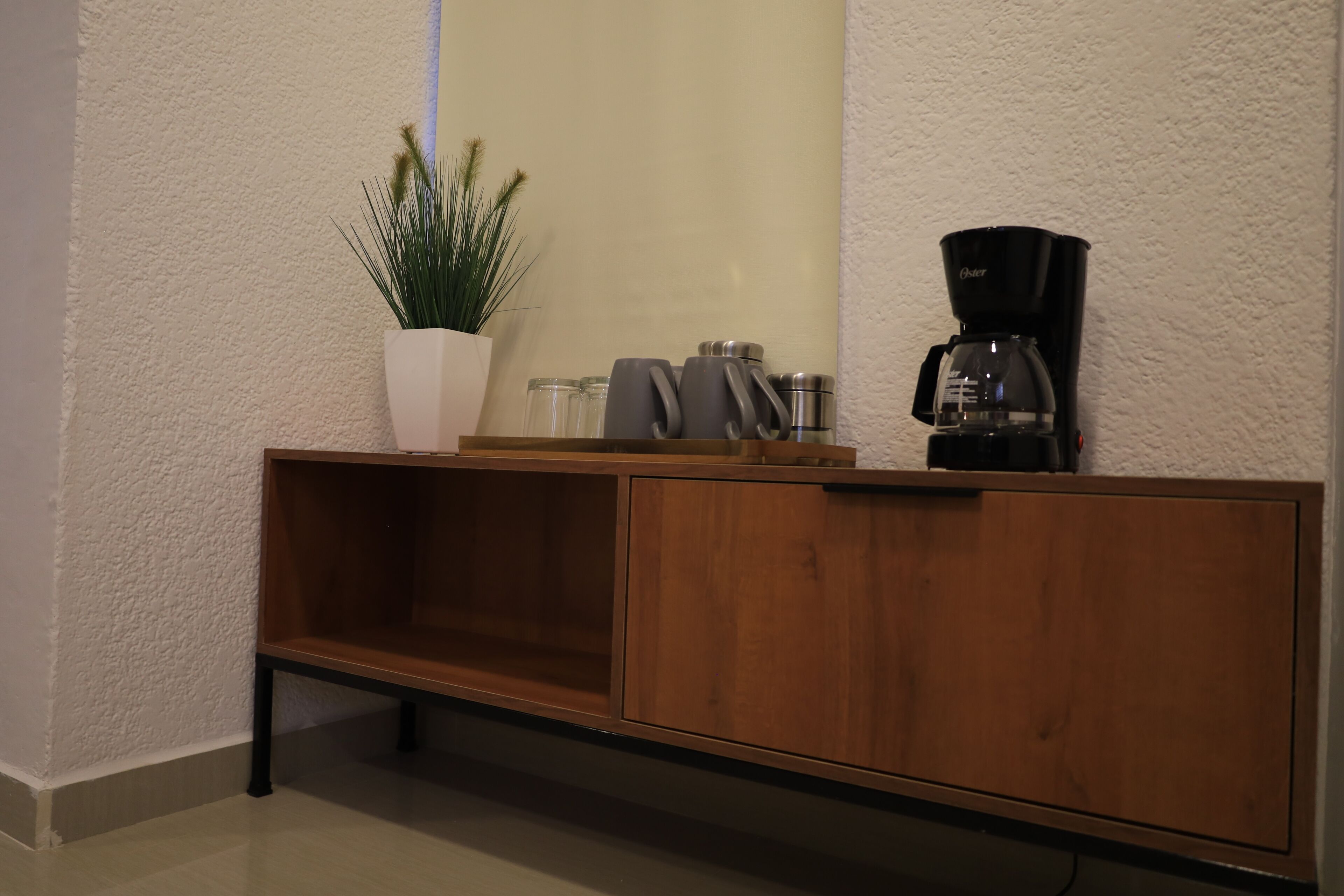 A wooden cabinet with a potted plant, a coffee maker, and glass containers.