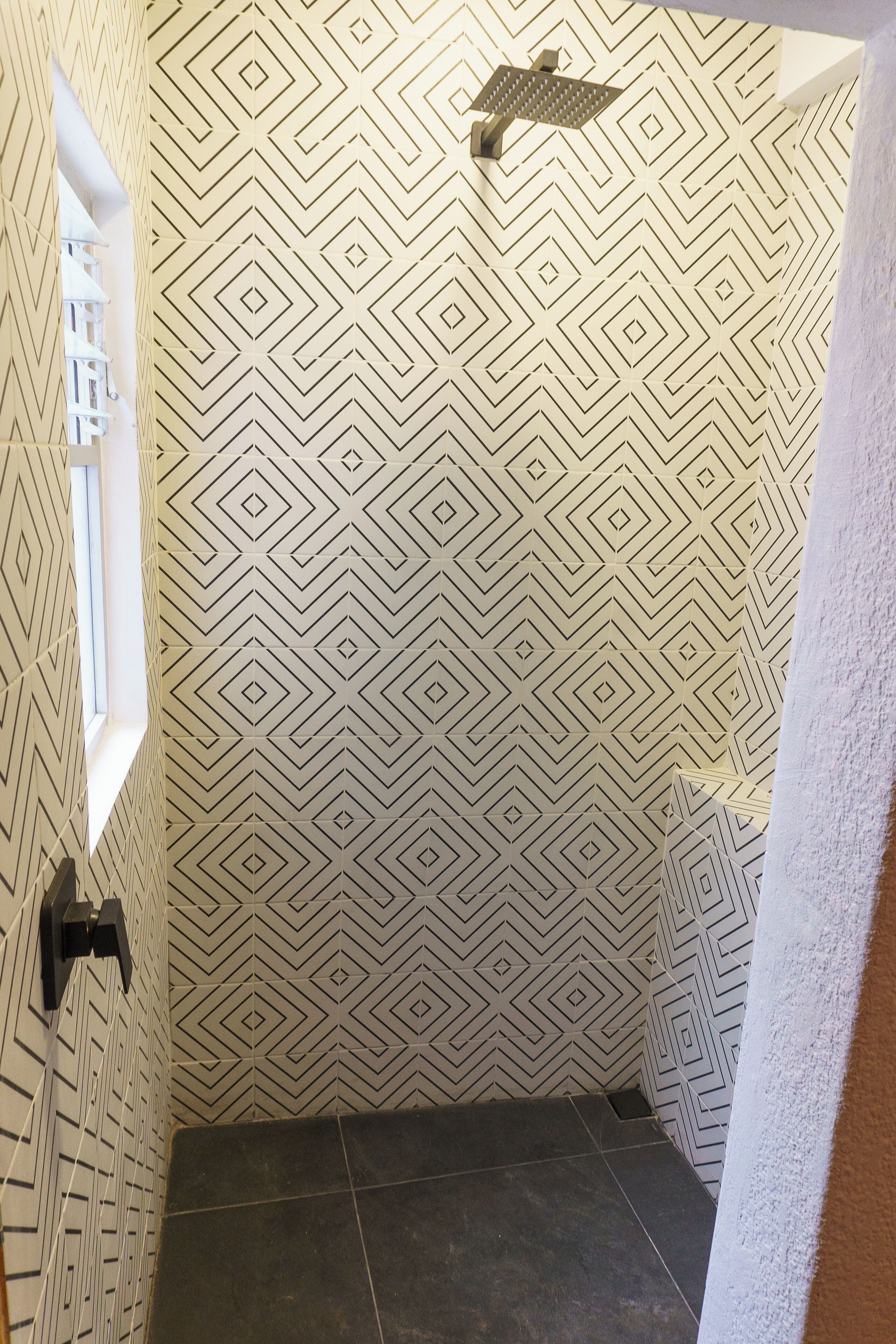 A bathroom with a geometric patterned wall, a showerhead, and a window.