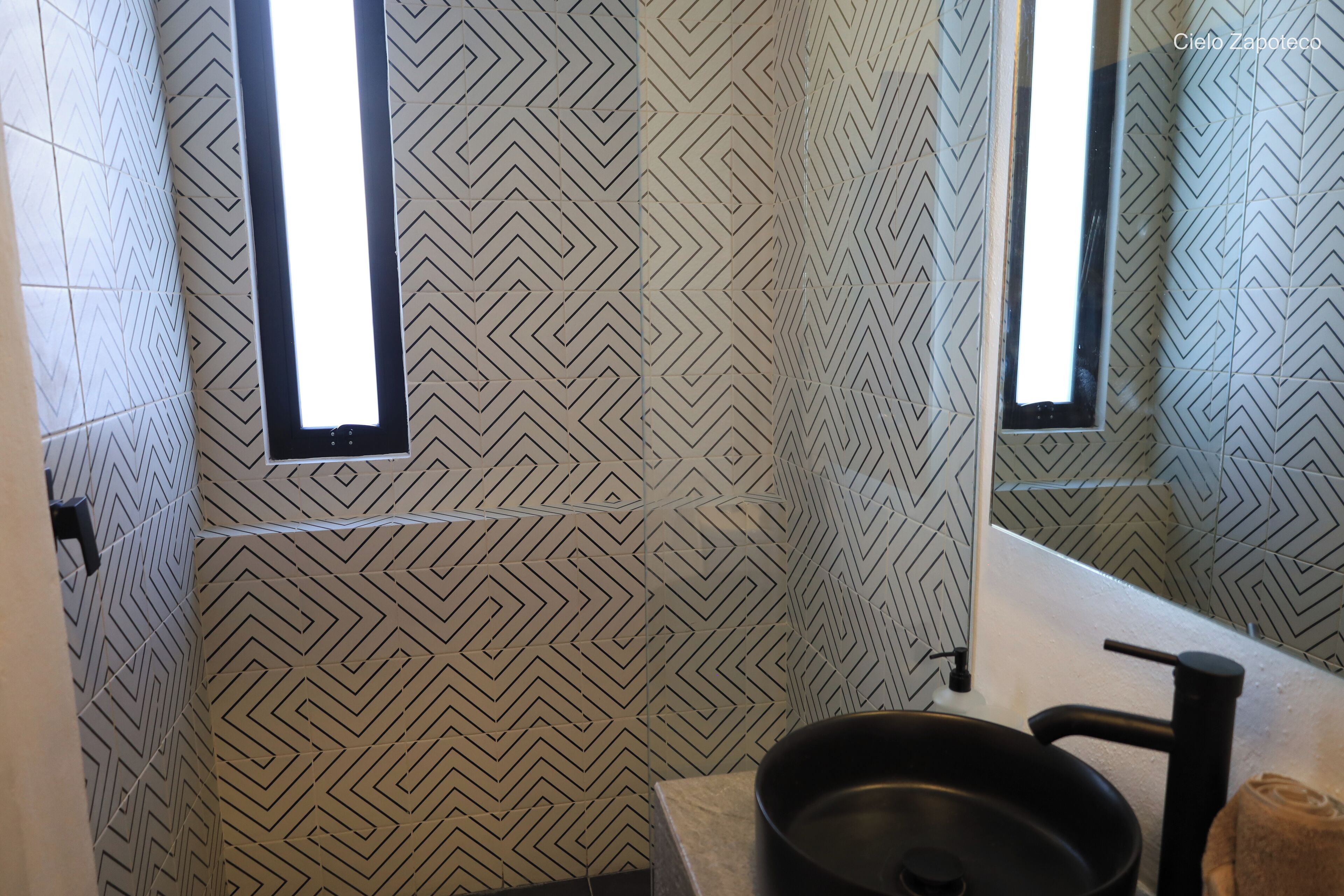Een badkamer met een wand met een geometrisch patroon, een wastafel met een zwarte kom en een spiegel.