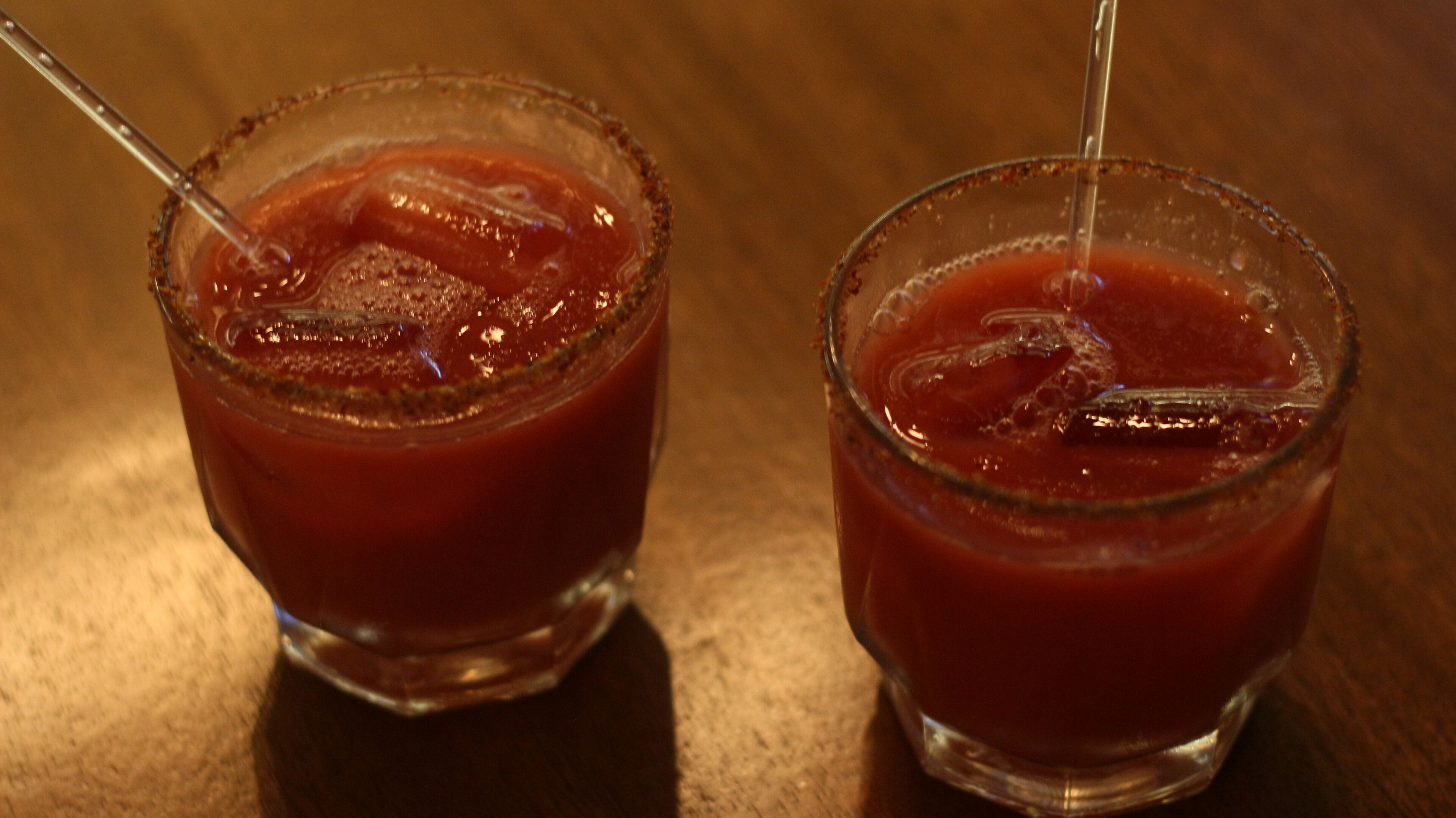 Dos vasos de bebida roja con cubitos de hielo y pajitas sobre una superficie de madera.