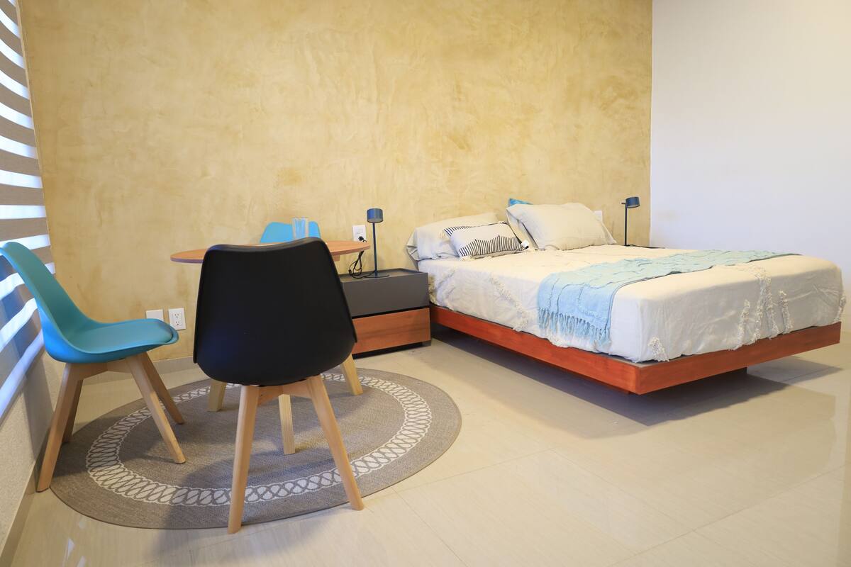 Um quarto com cama, escrivaninha, cadeira e abajur.