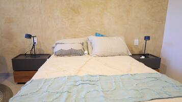 Un letto rifatto con cura, una coperta blu, due comodini con lampade e un muro con texture.