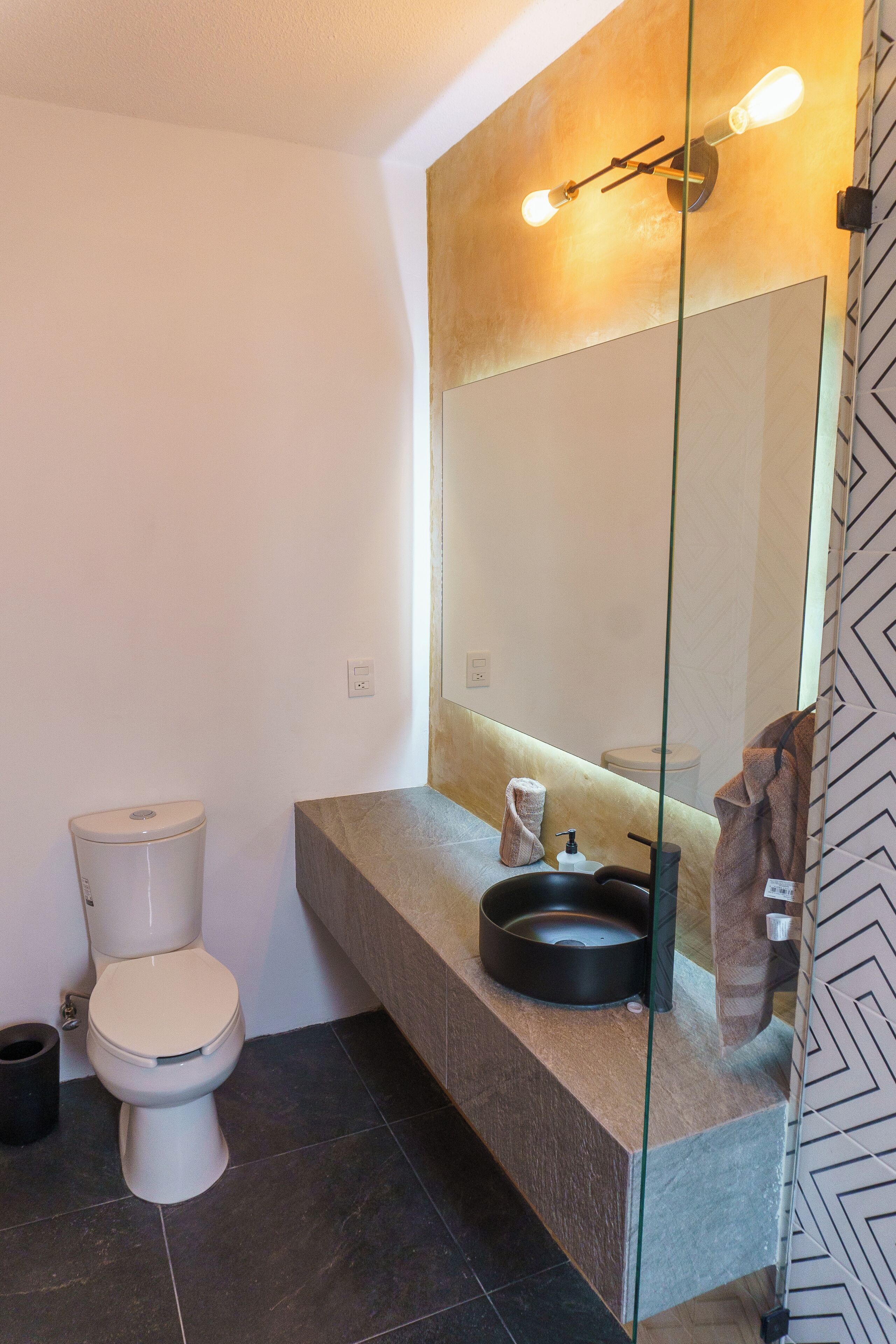 A modern bathroom with a toilet, a vanity with a mirror, and a glass partition.
