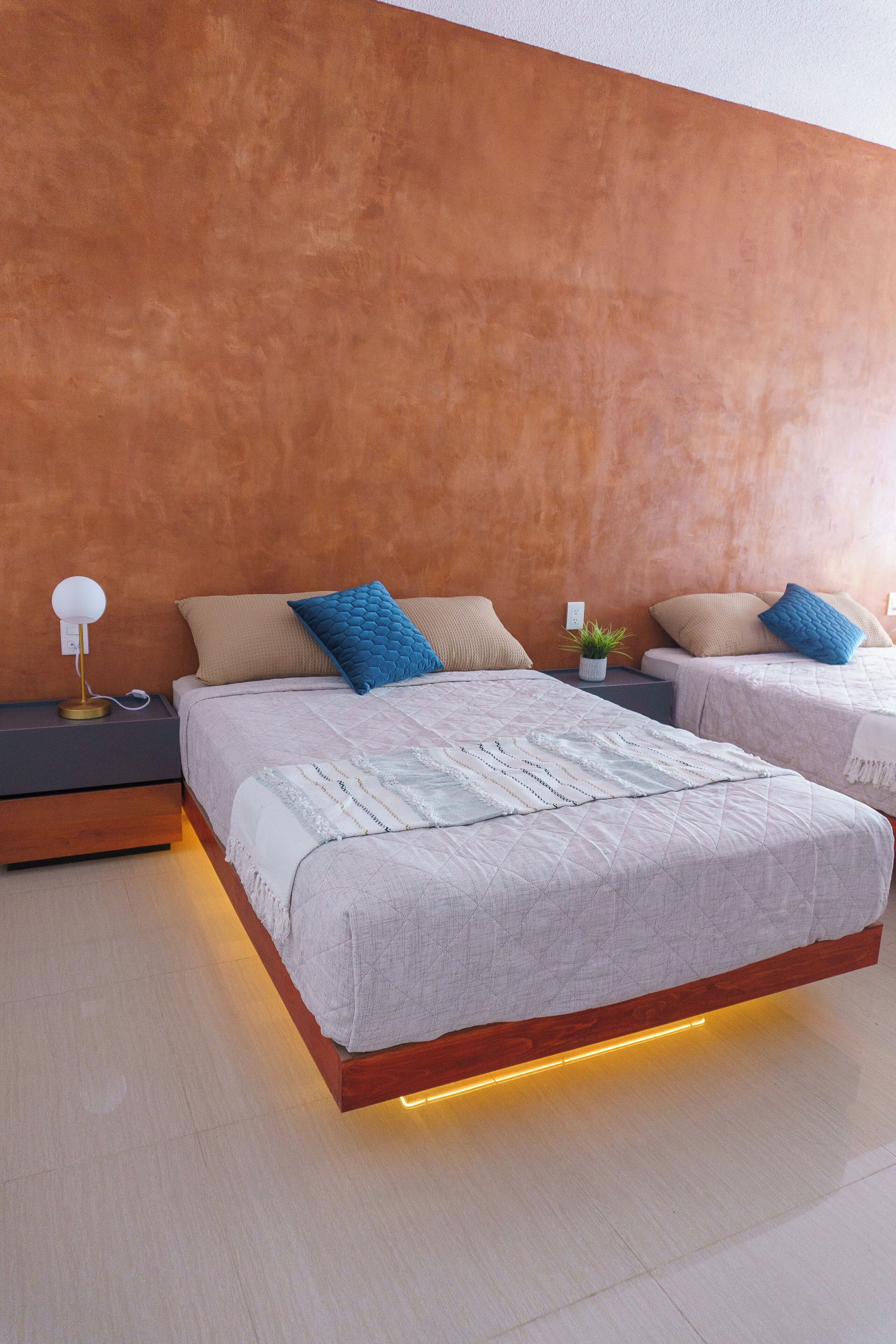 A modern bedroom with two beds, a nightstand, and a bedside table with a lamp.