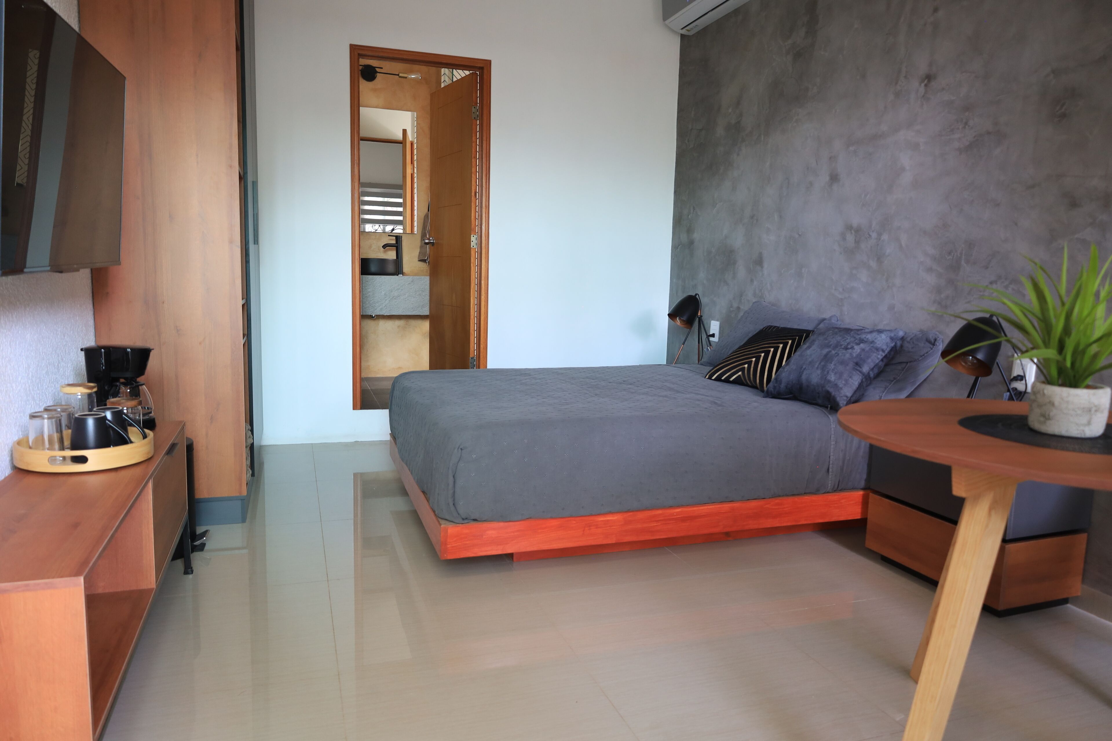 A modern bedroom with a bed, bedside table, and a small round table with a plant.