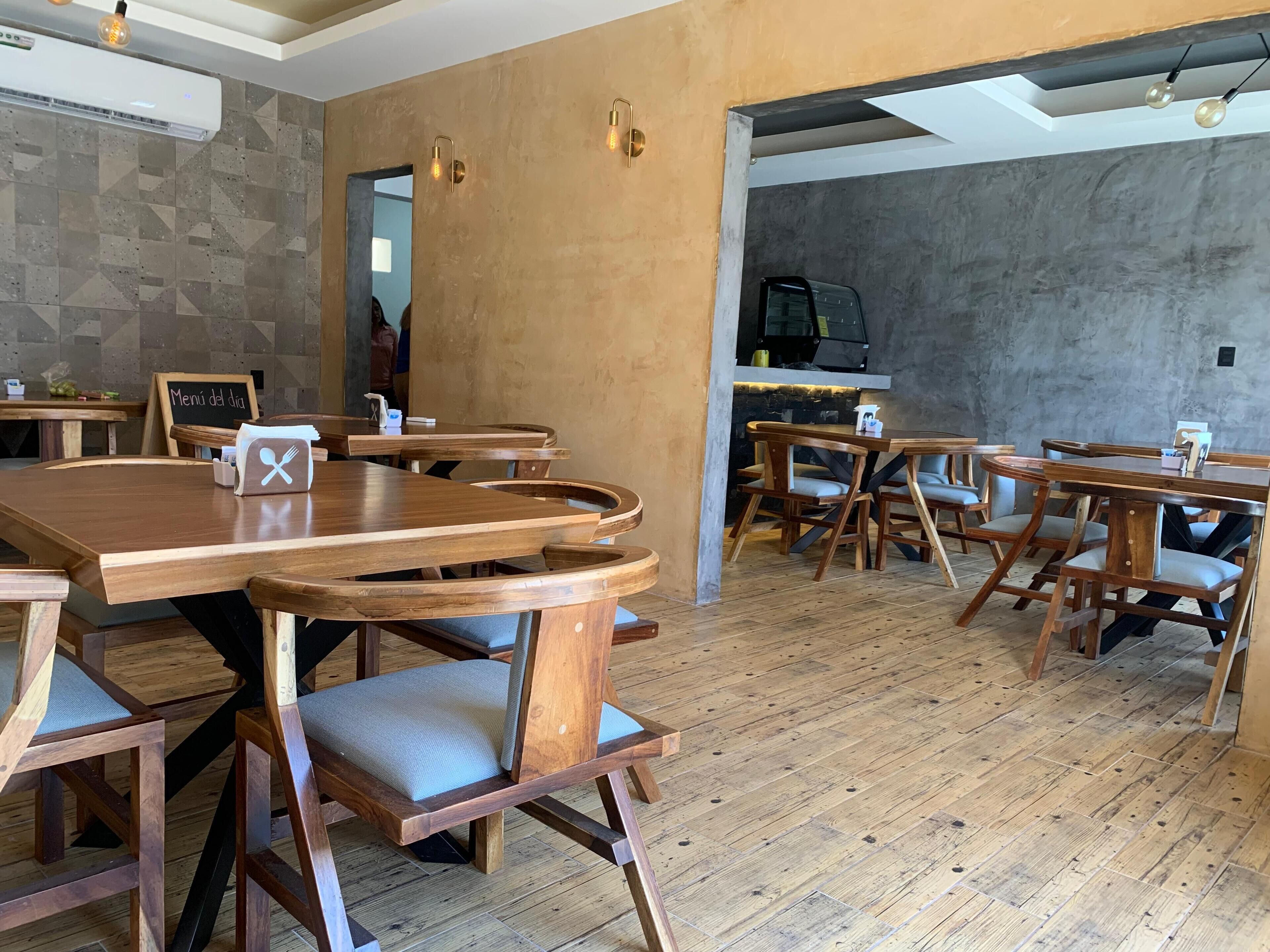 Interior de restaurant amb taules i cadires de fusta, un menú a la pissarra i una zona de bar.