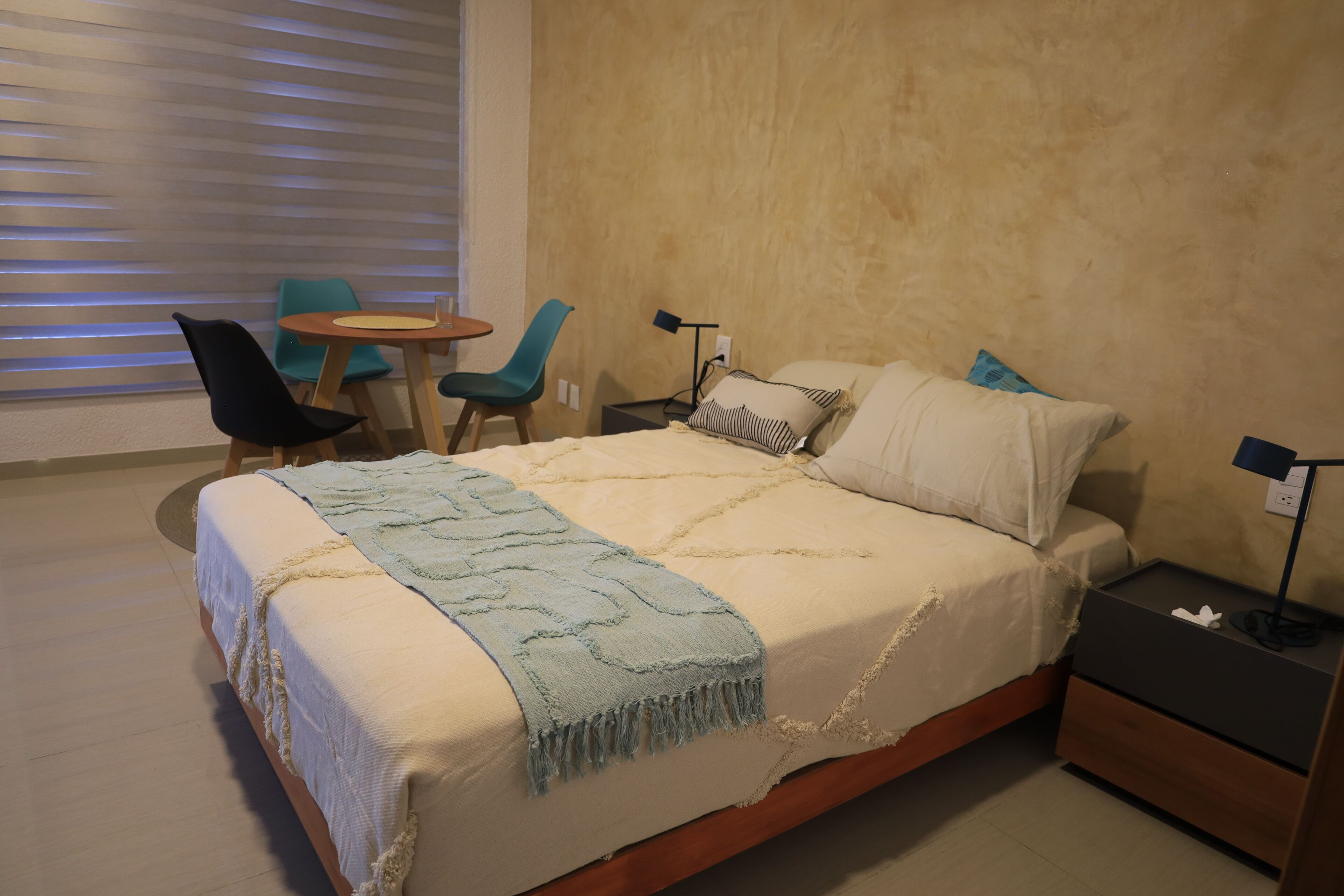 A bedroom with a bed, bedside tables, a chair, a small table, and a lamp.