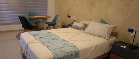 A bedroom with a bed, bedside tables, a chair, a small table, and a lamp.