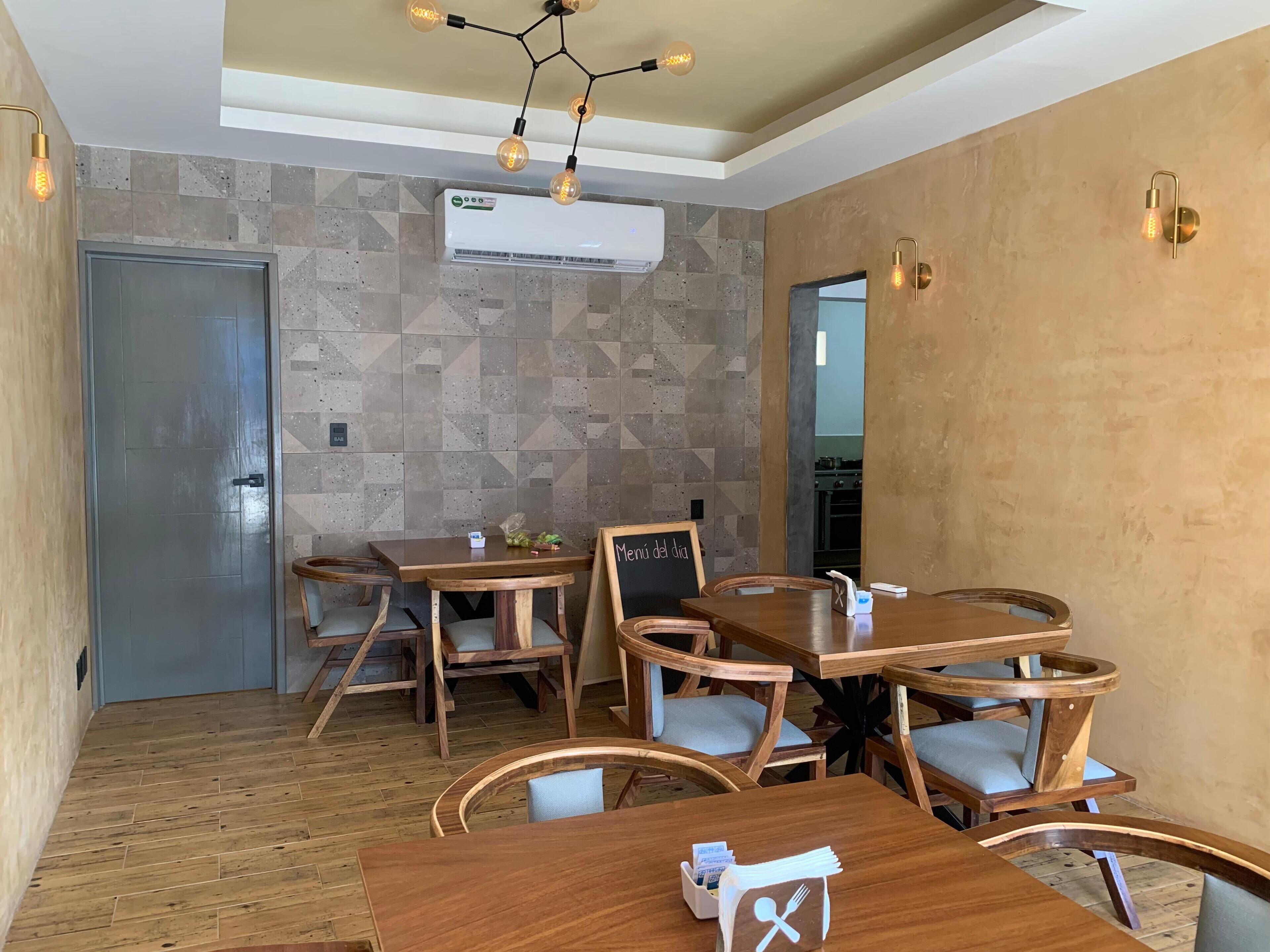 A dining area with wooden tables and chairs, an air conditioning unit on the wall, and a modern light fixture.