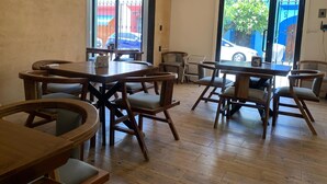 Un café amplio con mesas y sillas de madera, ventanas grandes que dan a la calle y una lámpara de techo moderna.