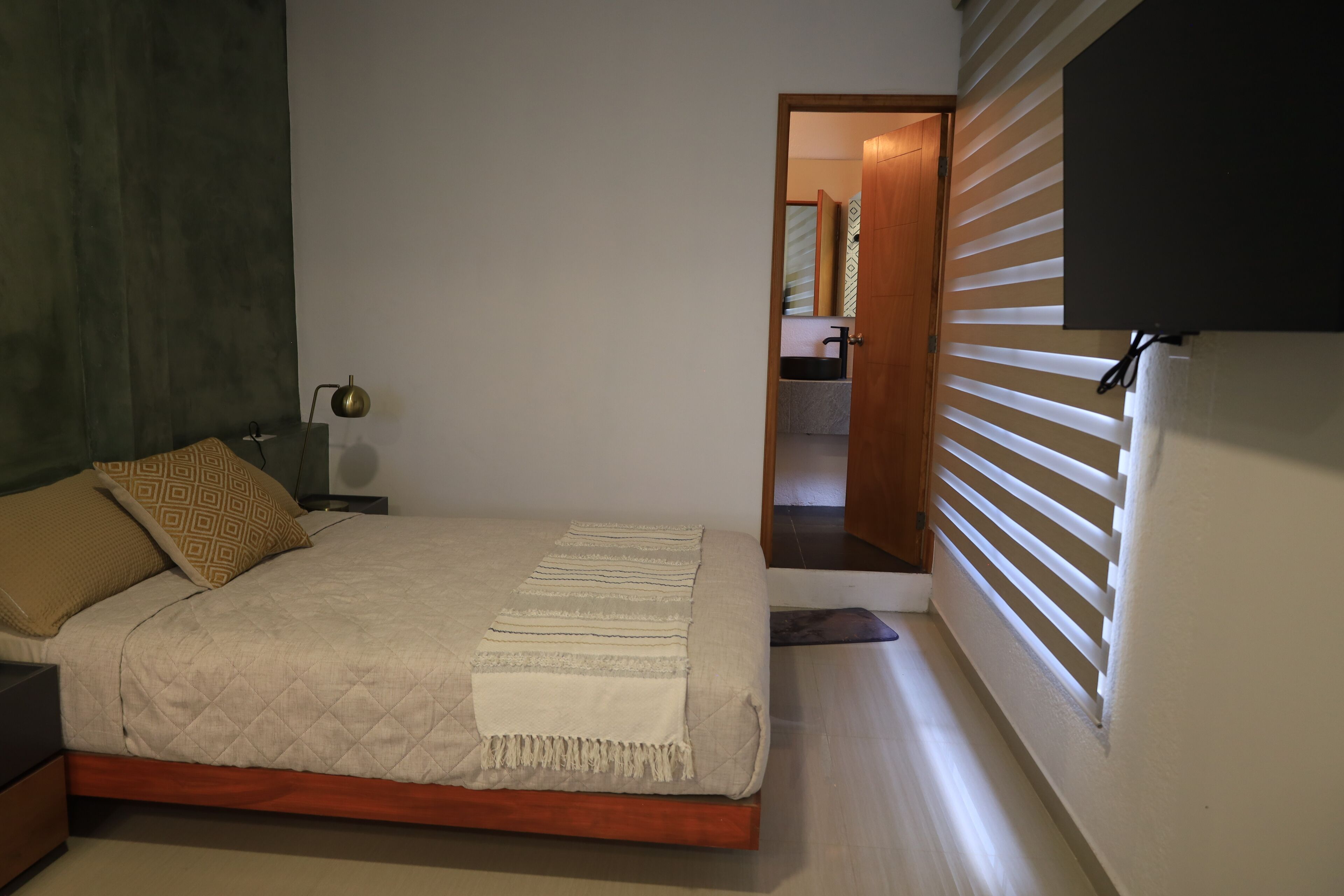 A bedroom with a bed, bedside table, lamp, and a view of a bathroom through an open door.