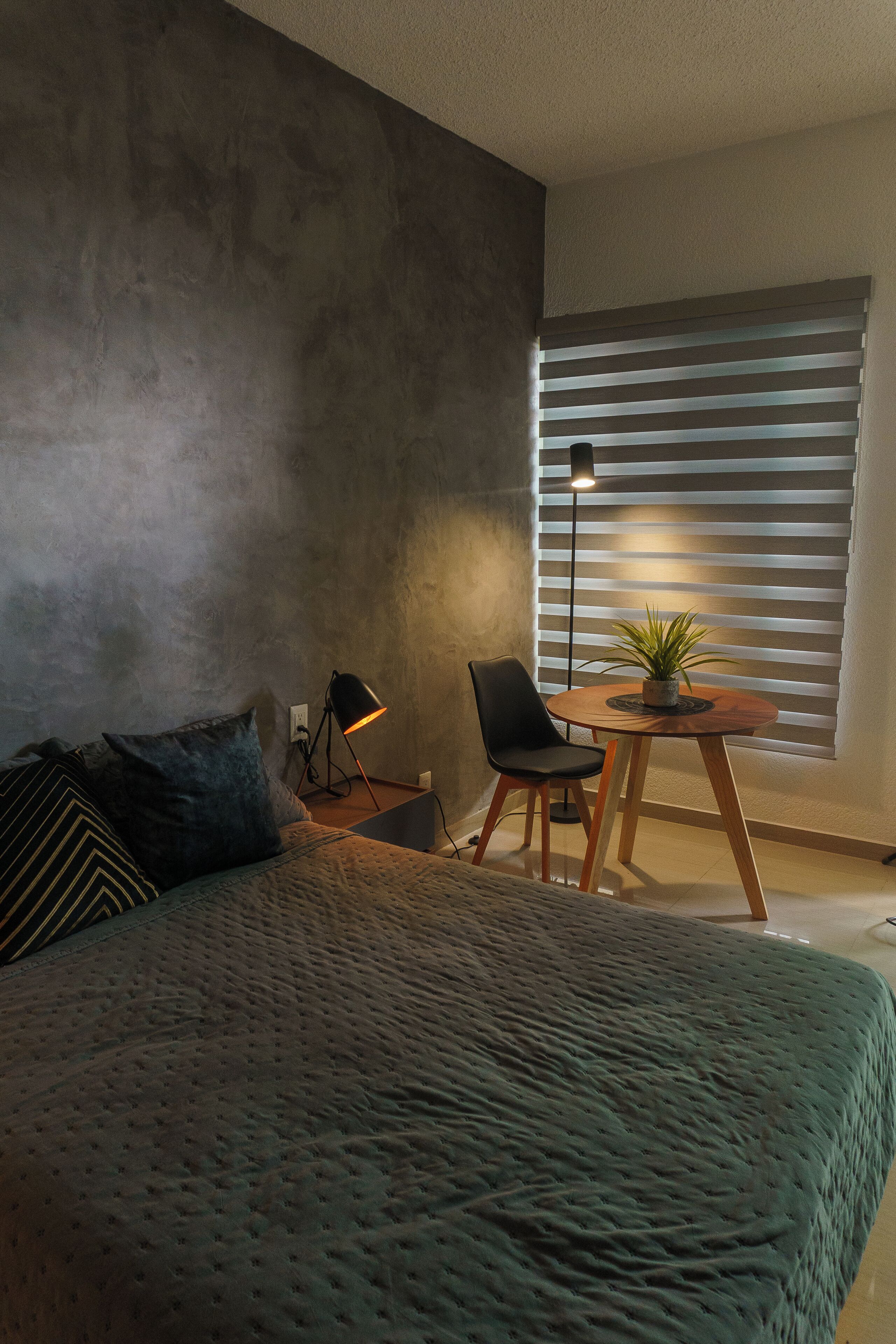 Une chambre à coucher comprenant un lit, un bureau, une chaise, une lampe et une fenêtre avec des stores.