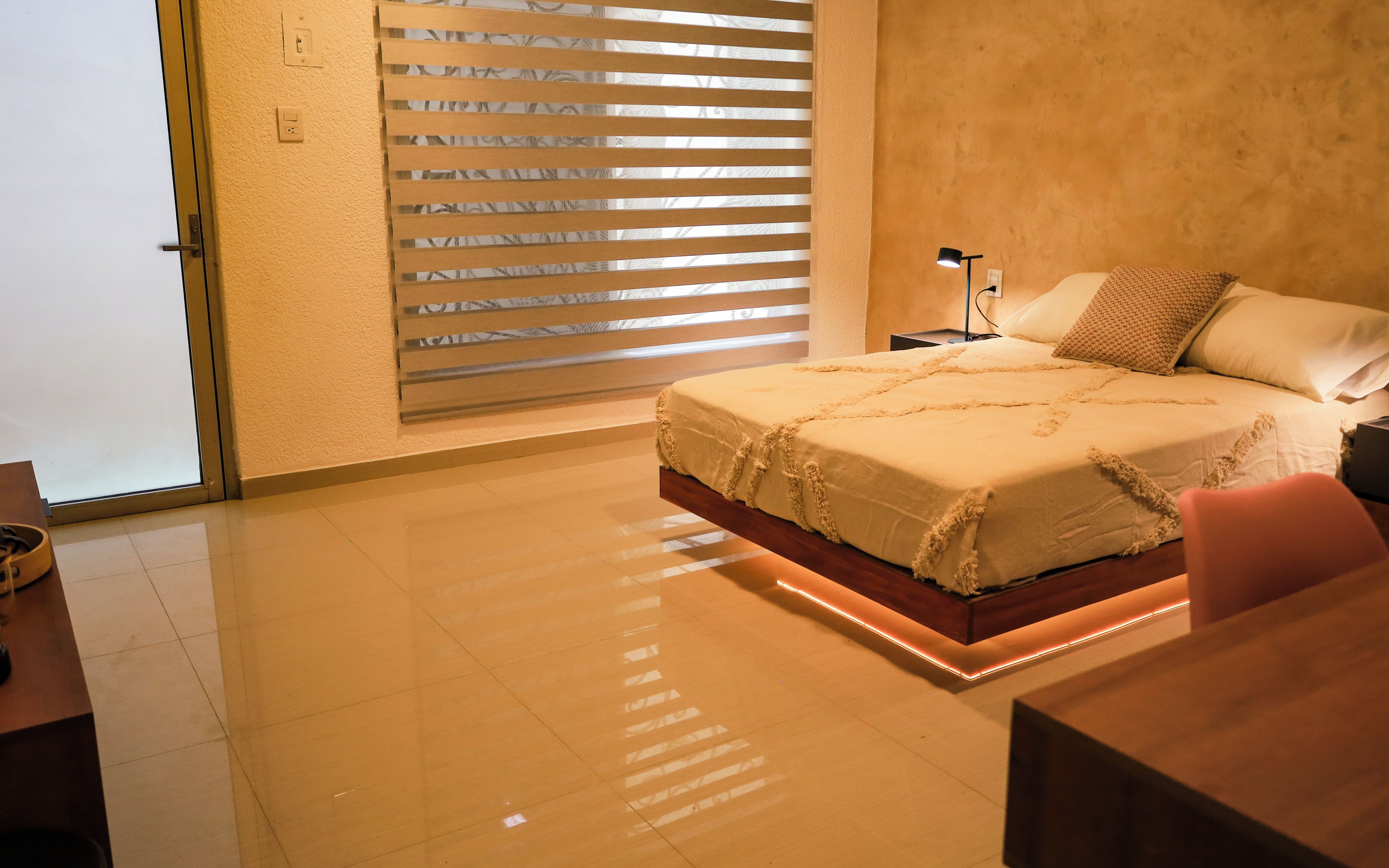 A bedroom with a bed, bedside table, lamp, and a window with blinds.