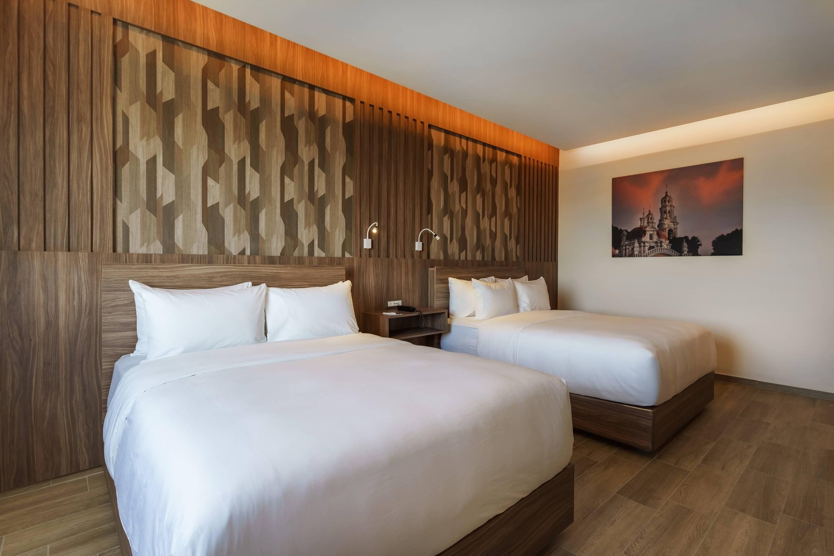 A hotel room with two beds, wooden paneling, a nightstand, and a painting on the wall.