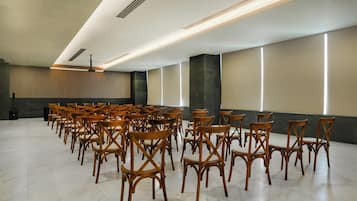 Uma sala de conferências com fileiras de cadeiras de madeira, palco com um púlpito e teto moderno com iluminação embutida.