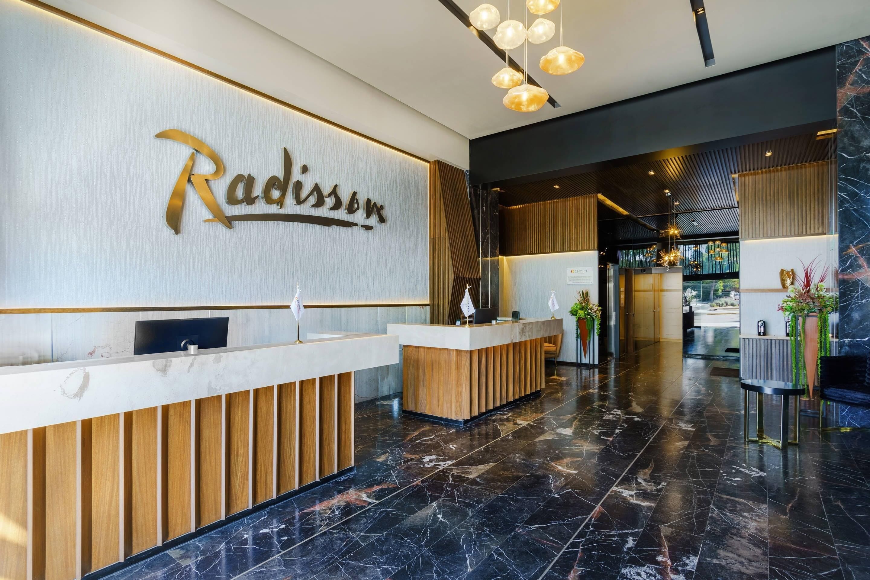 Un espace d’accueil doté d’un sol en marbre, d’un comptoir en bois et d’une enseigne fixée au mur sur laquelle on peut lire « Radisson ».
