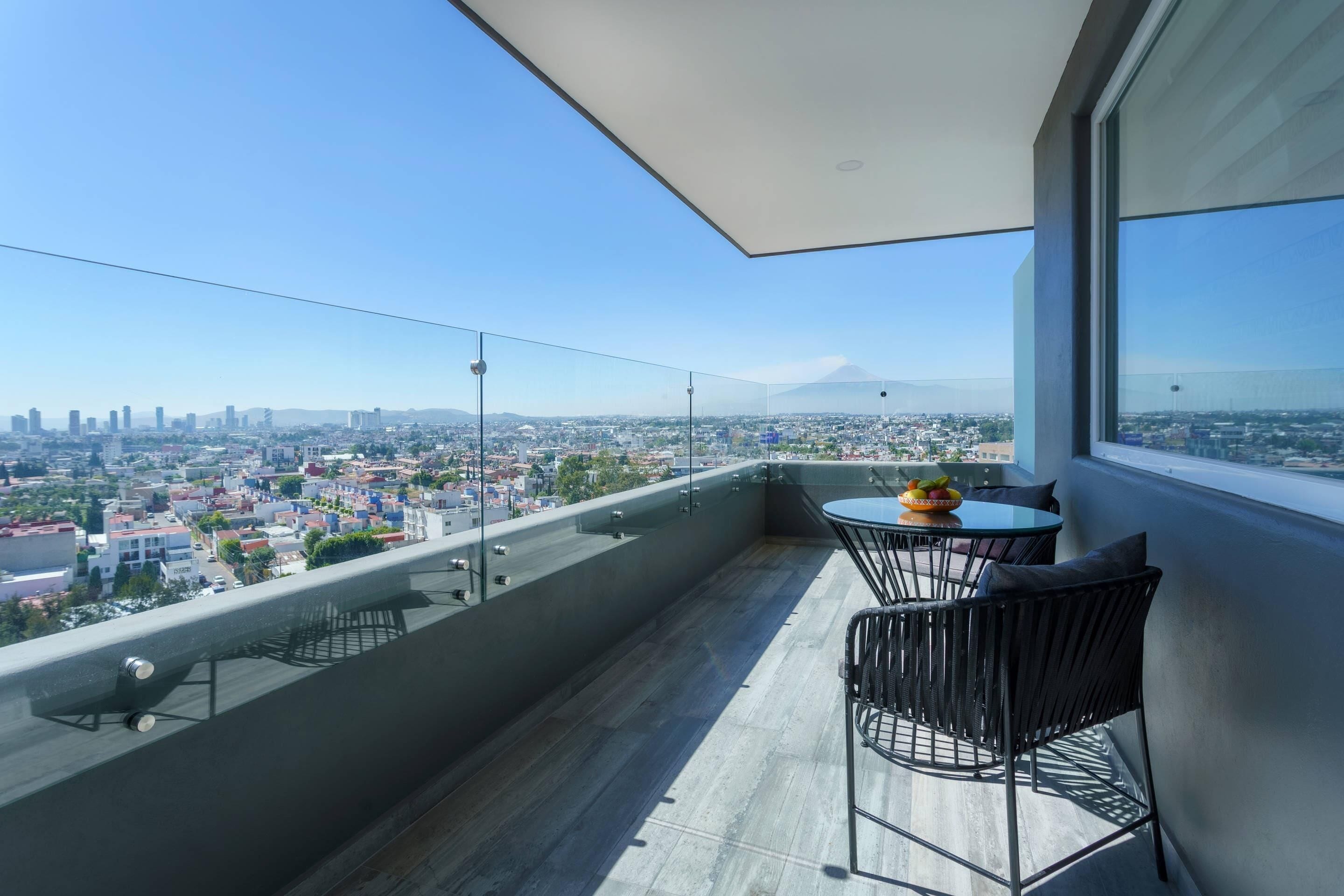 Un balcón con vista a la ciudad, una mesa con sillas y un frutero.