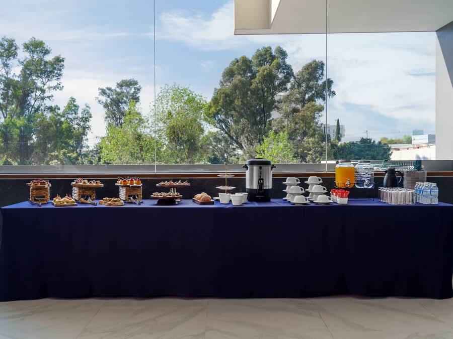 Una mesa de buffet con diversos alimentos y bebidas, con árboles y un cielo despejado de fondo.