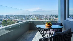 A balcony with a glass railing, a round table with chairs, and a bowl of fruit. - Radisson Puebla Angelopolis (Puebla)
