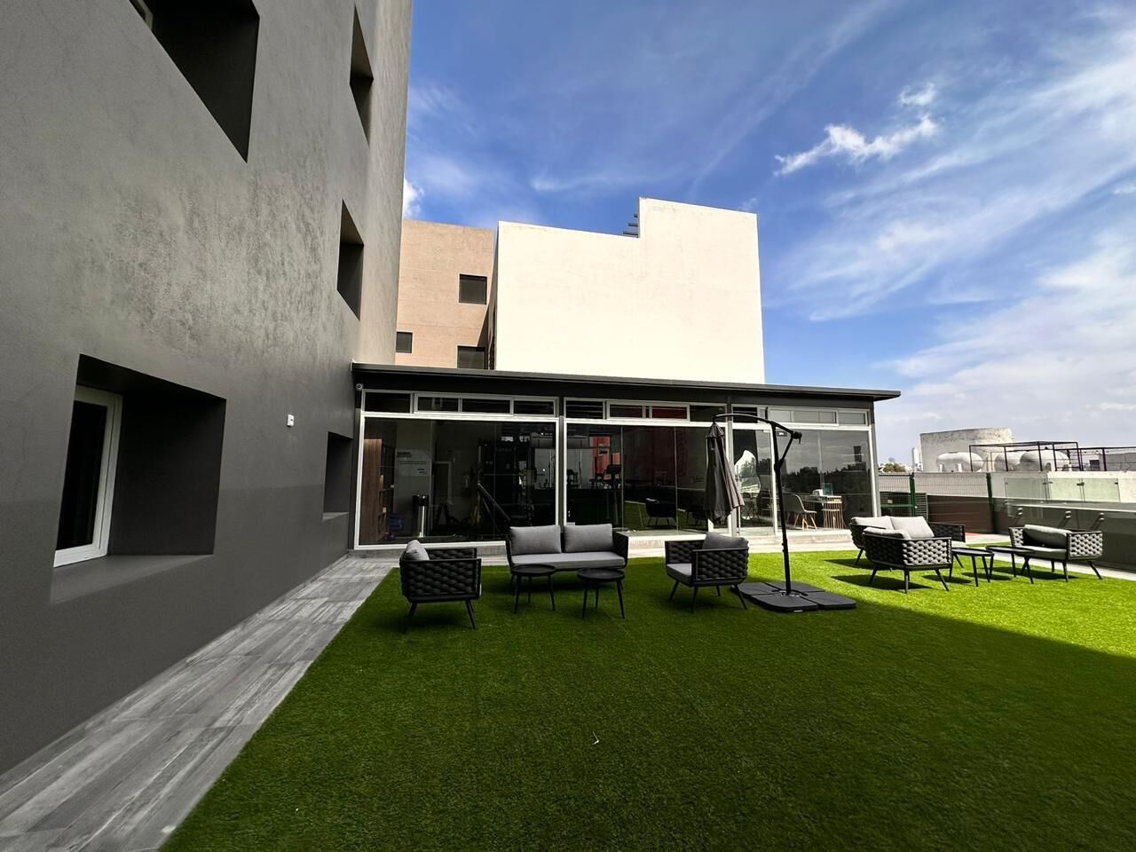 A modern building with a flat roof, large windows, and a patio area with outdoor furniture.