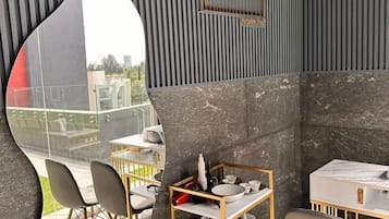 Ein modernes Interieur mit einem gewölbten Spiegel, der einen Essbereich widerspiegelt, einer goldrahmigen Ablage mit Geschirr und einem an der Wand befestigten Schild mit Buchstaben.