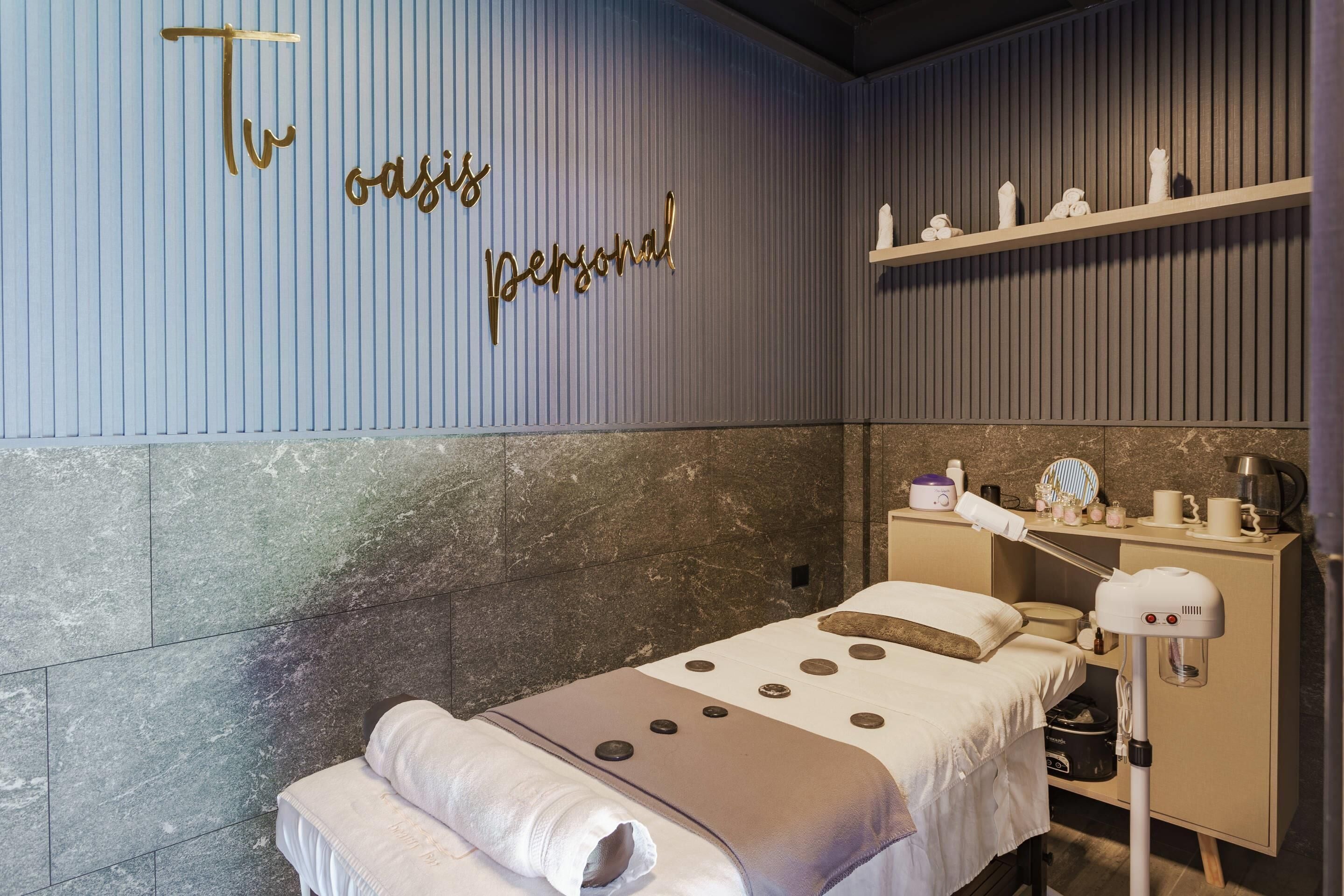 Una habitación moderna con una cama, un sillón de masajes, un tocador con artículos de aseo y una pared decorada con un cartel.