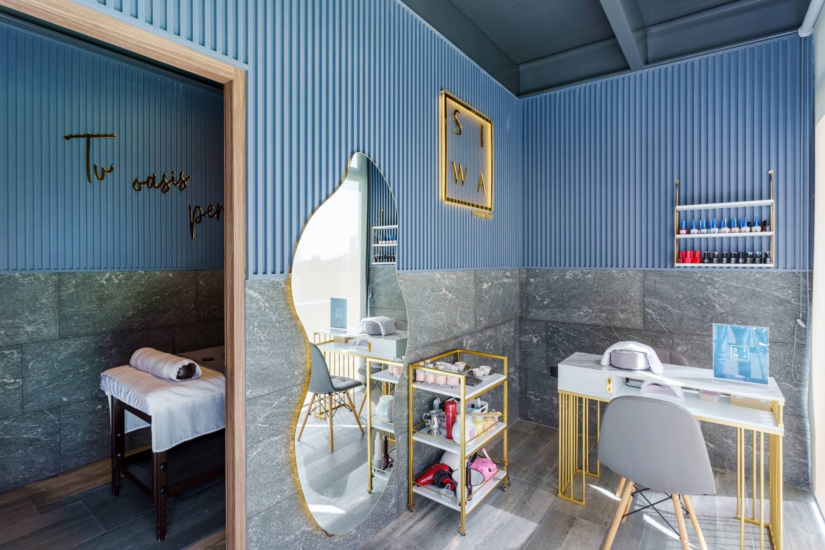 A room with a massage chair, a desk with a computer, a shelf with bottles, and a mirror.