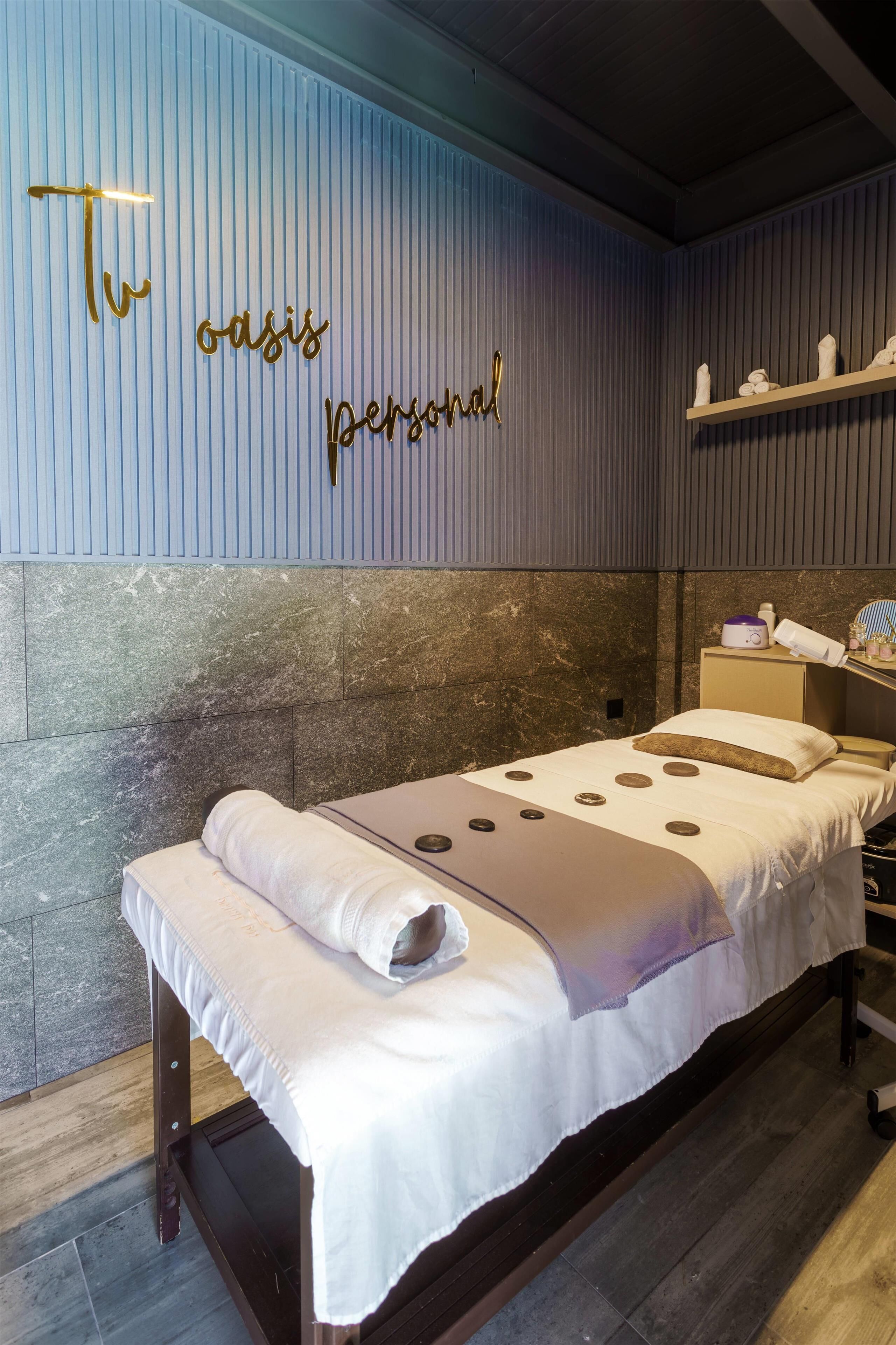 A room with a bed, a wall-mounted shelf with towels, and a decorative sign.