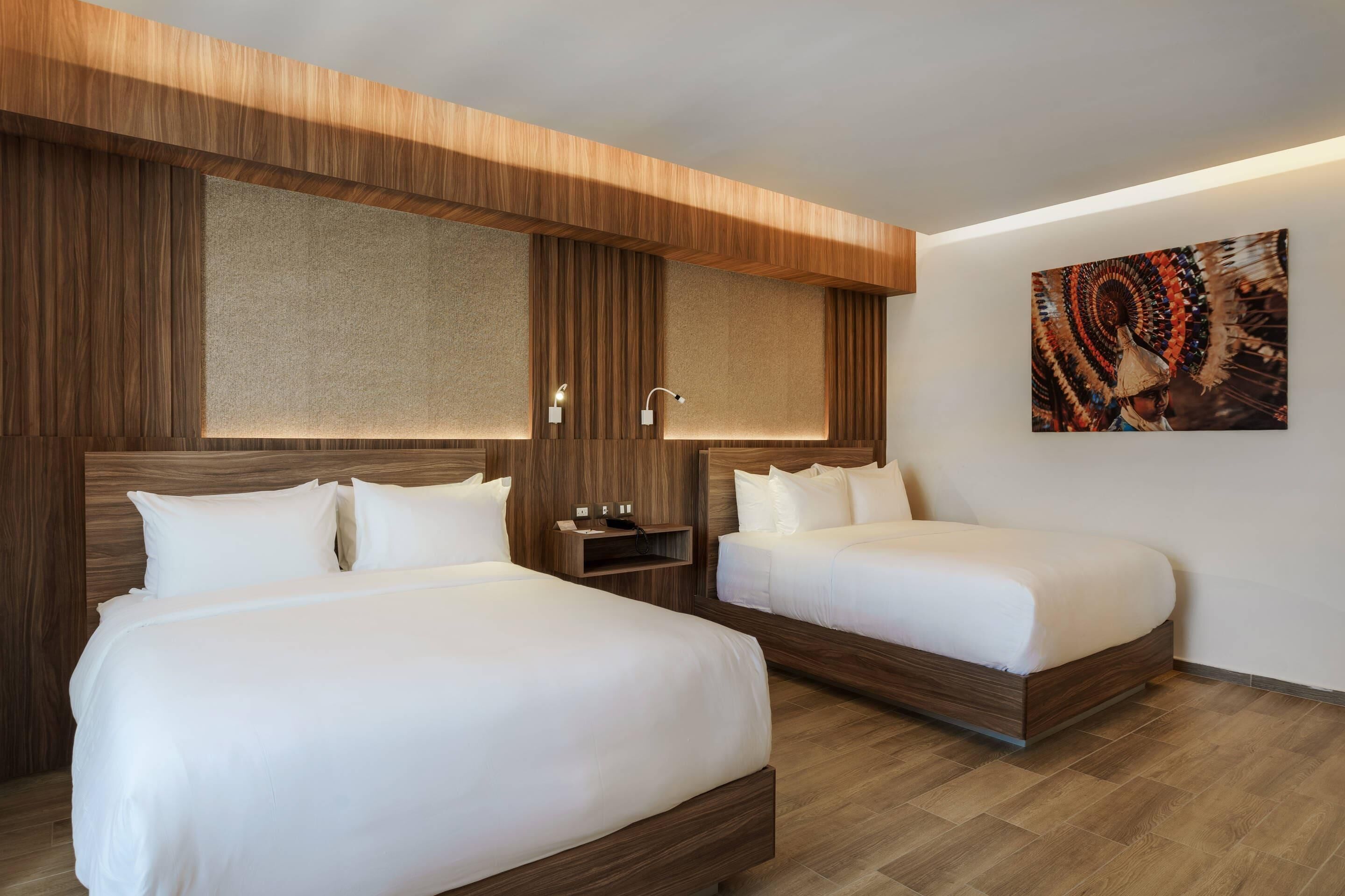 A hotel room with two beds, wooden headboards, a wall-mounted TV, and a painting.