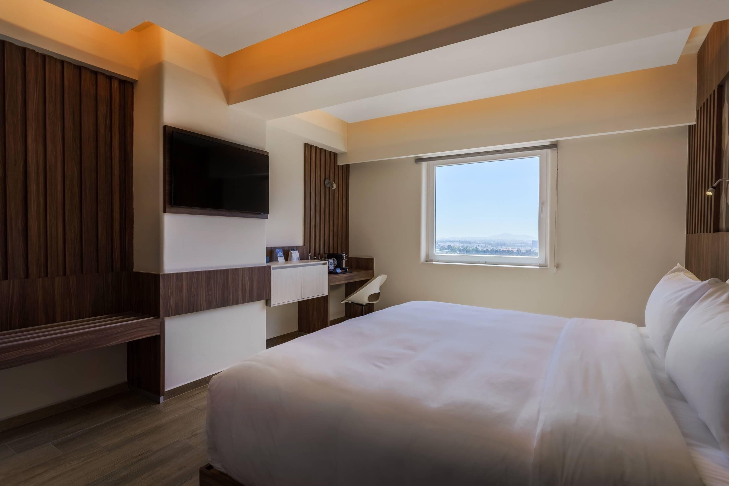 Una camera d'hotel con un letto, una scrivania, una TV e una finestra vista città.